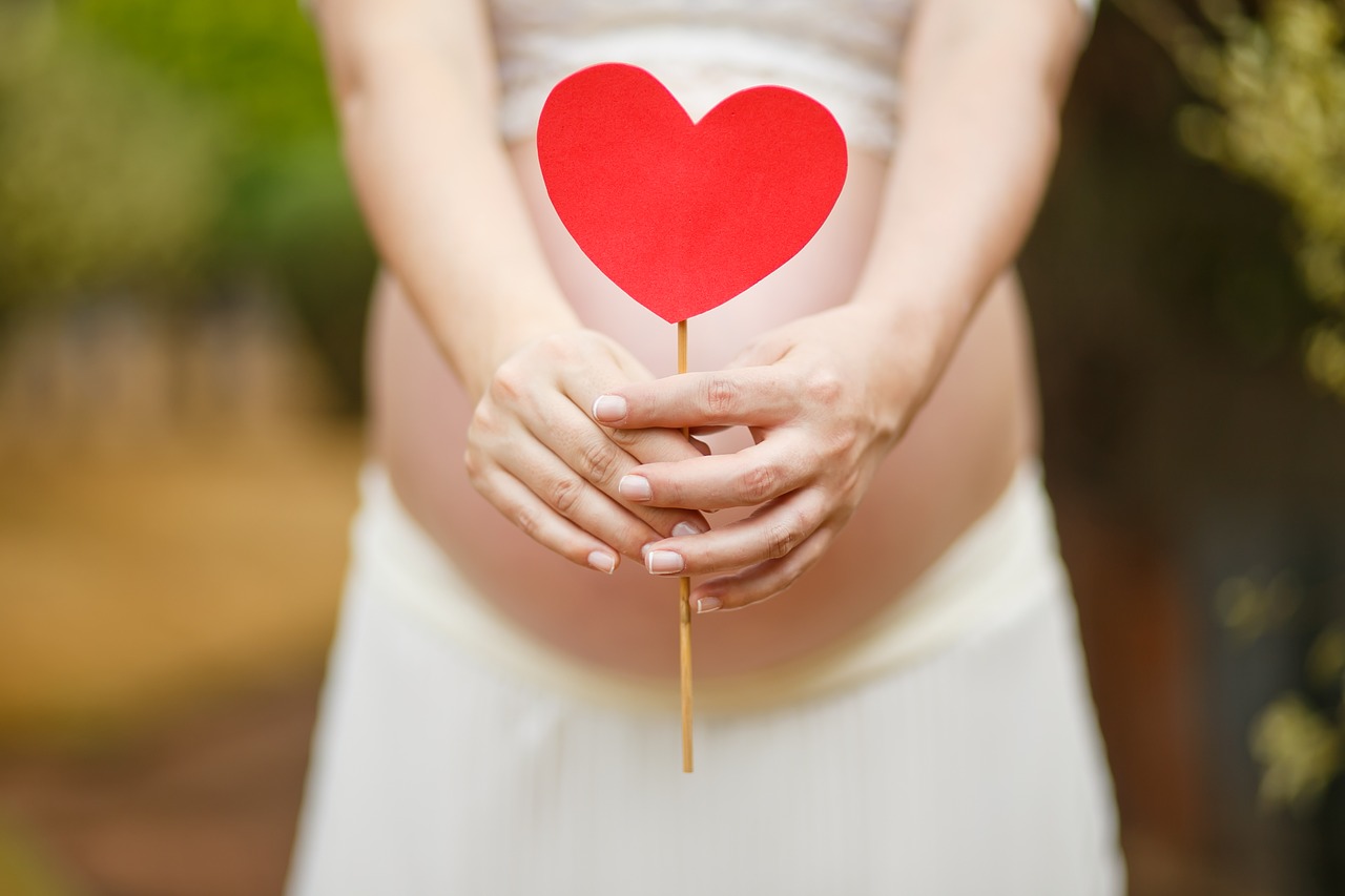 Femme enceinte tenant son ventre arrondi en extérieur, dans une lumière douce